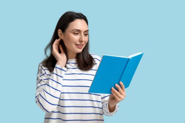 Genç ve güzel bir kadın mavi arka plan üzerine kitap okuyor.