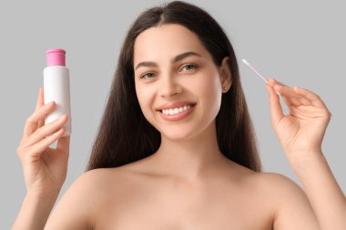 Pamuk tomurcuğu ve gri arka planda bir şişe mikiler suyu olan güzel, genç ve mutlu bir kadın.