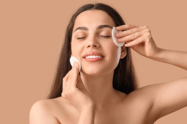 Pamuk yastıklı güzel, genç bir kadın kahverengi arka plandaki makyajı temizliyor.