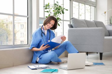 Klinikte pencerenin yanında panosu olan bir kadın stajyer.