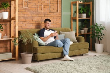 Genç yakışıklı adam bitkilerle dolu bir odada cep telefonu kullanıyor.