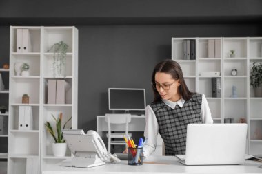 İşyerinde dizüstü bilgisayarla çalışan genç bir kadın şık bir ofiste çalışıyor.