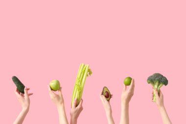 Yeşil meyveli eller ve pembe arka planda sebzeler