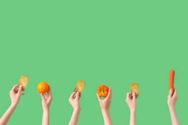 Yeşil arka planda taze sebzeli, turuncu ve kredi kartlı eller