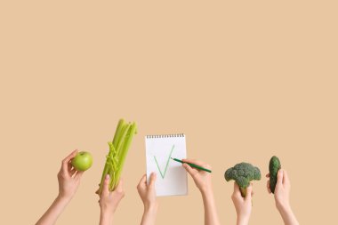 Ellerinde yeşil elma, sebze ve bej arkaplan işaretli defter var.