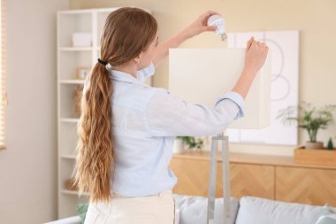 Genç bir kadın ampulü evdeki lambaya vidaladı.