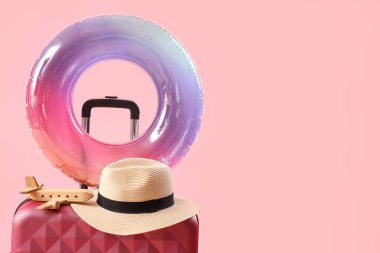 Şişirilebilir halka ve bavul içinde ahşap uçak ve pembe arka planda şapka. Seyahat kavramı