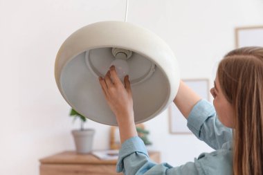 Evdeki tavan lambasına ampul takan genç bir kadın, yakın plan.