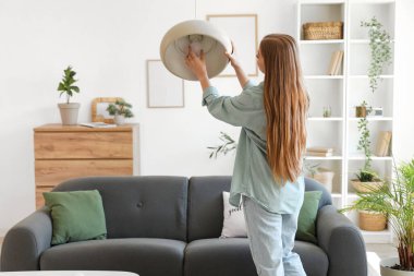 Genç bir kadın evdeki tavan lambasına ampul takıyor.