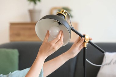 Evde ampulü lambaya takan genç bir kadın, yakın plan.