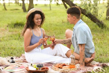 Güzel, genç ve mutlu bir çift, bir kadeh şarapla parkta romantik bir piknik yapıyorlar.