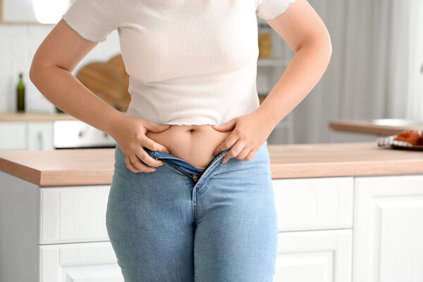 Young woman in tight jeans at home, closeup. Weight gain concept