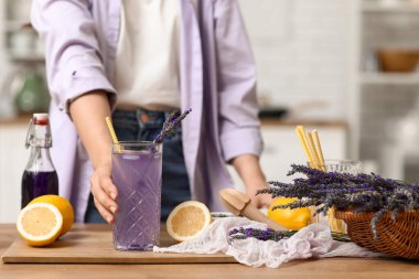 Mutfaktaki masada elinde bir bardak taze lavanta limonatasıyla genç bir kadın.