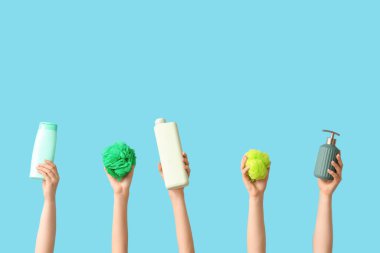 Mavi arka planda kozmetik ürünler ve banyo süngerleriyle dolu kadın elleri.