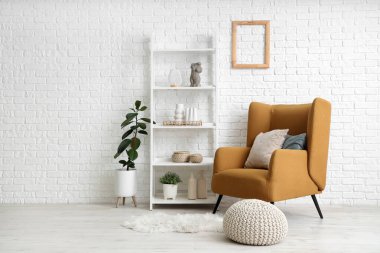 Beyaz tuğla duvarın yanında rahat koltuğu ve raf ünitesi olan modern bir oda.