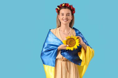 Mavi arka planda Ukrayna bayrağı, ayçiçeği ve çiçek çelengi olan güzel genç bir kadın.