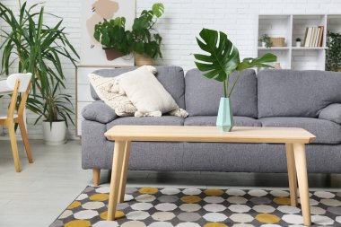 Masada ve şık koltukta tropikal canavar yaprakları olan modern bir oturma odası.