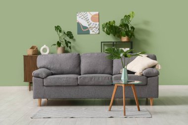 Masada ve şık koltukta tropikal canavar yaprakları olan modern bir oturma odası.