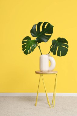 Sarı duvarın yanındaki masada vazo yaprakları vardı.