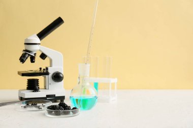 Mikroskop ve böğürtlenli profesyonel laboratuvar bardakları sarı duvarın yanındaki masada.