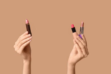 Kahverengi arka planda farklı ruj izleri olan kadın elleri.