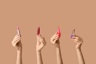 Kahverengi arka planda bir sürü ruju olan kadın elleri.