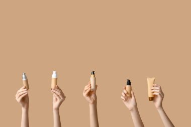 Şişeli kadın elleri ve kahverengi arka planda makyaj malzemeleri var.