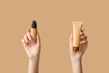 Kahverengi arka planda şişe ve makyaj malzemesi olan kadın elleri.