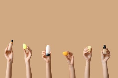 Makyaj temeli ve kahverengi arka planda süngerleri olan kadın elleri.