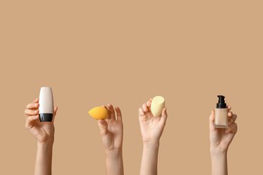 Makyaj temeli ve kahverengi arka planda süngerleri olan kadın elleri.