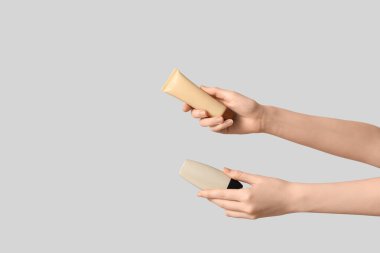 Gri arkaplanda makyaj tüpleri olan kadın elleri