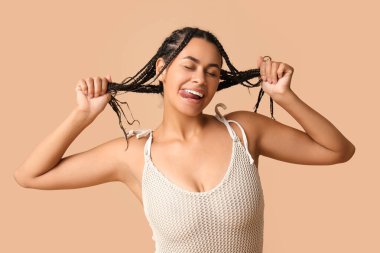 Kahverengi arka planda dilini gösteren şık hasır mayo giymiş güzel bir Afro-Amerikalı kadın.