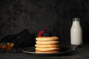Taze böğürtlenli krep, kırmızı frenk üzümü ve siyah arka planda bir şişe süt.