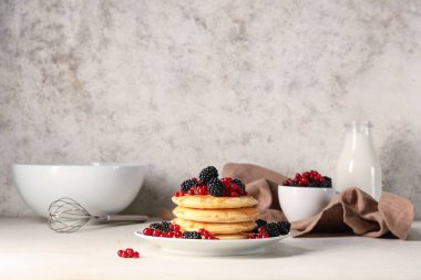 Taze böğürtlenli krep, kırmızı frenk üzümü ve beyaz arka planda bir şişe süt.