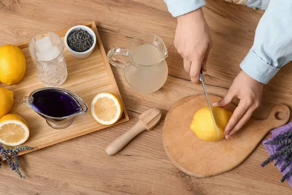Ahşap masada lavantalı limonata hazırlamak için limon kesen genç bir kadın.