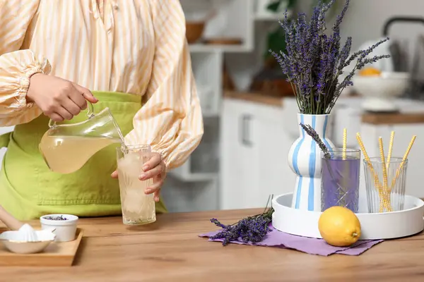 Mutfaktaki masada lavanta limonatası hazırlamak için limon suyunu bardağa dolduran genç bir kadın.