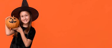 Cadılar Bayramı 'nda cadı gibi giyinmiş, turuncu arka planda balkabağı olan ve mesaj atmak için yeri olan tatlı küçük bir kız.