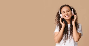 Bej arka planda kulaklıklı, mesaj atmak için yeri olan mutlu, Afro-Amerikalı bir kadın.