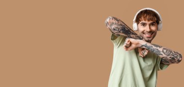 Kulaklıklı, kahverengi arka planda dans eden, mesaj için yeri olan dövmeli genç adam.