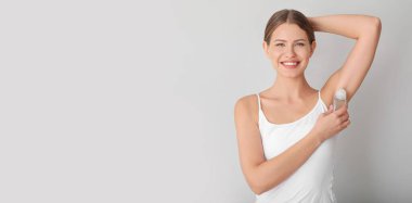 Gri arkaplanda deodorant kullanan genç bir kadın.