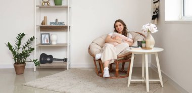 Oturma odasındaki koltukta oturan minderli genç kadın.