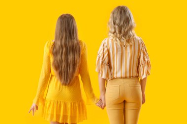 Sarı arka planda el ele tutuşan genç kız kardeşler.