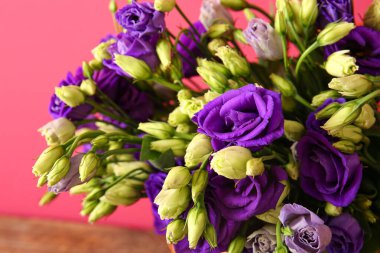 Kırmızı duvarın yanındaki ahşap masada Eustoma çiçekleri