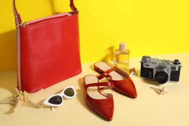Çantalı kırmızı sandaletler, güneş gözlüğü ve sarı duvarın yanındaki kamera.