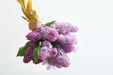 Beyaz duvarın yanında güzel leylak çiçeklerinden bir buket tutan kadın.