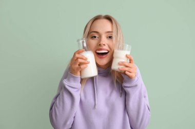 Yeşil arka planda bardak ve süt şişesi olan genç bir kadın.