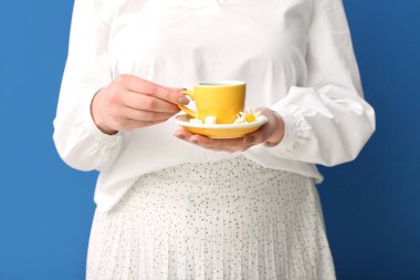 Mavi duvarın yanında bir fincan papatya çayı ve çiçeklerle güzel genç bir kadın.