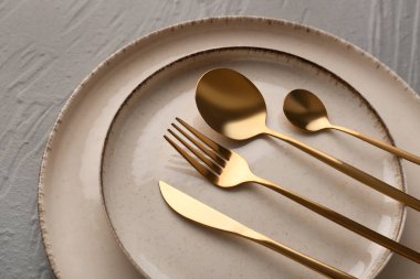 Gri arka planda bej plakalı altın çatal bıçak takımı.