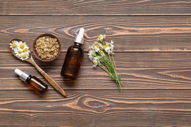 Gerekli yağ şişeleri, taze ve kurumuş papatya çiçekleri ahşap arka planda.
