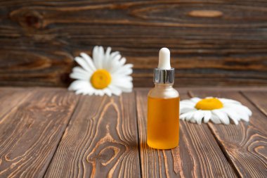 Bir şişe gerekli yağ ve ahşap arka planda taze papatya çiçekleri.